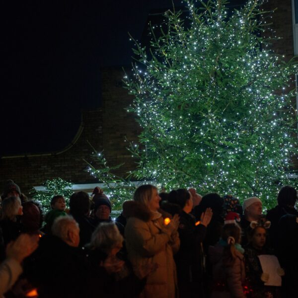 Christmas trees lit up with people holding candles in front of it