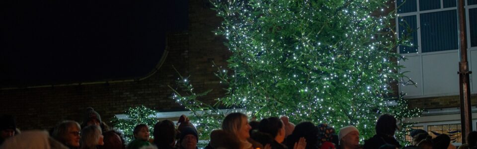 Christmas trees lit up with people holding candles in front of it