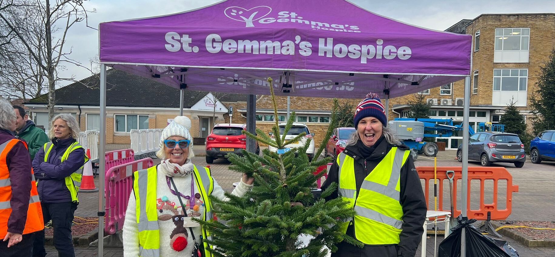 Two volunteers holding up a christmas tree in front of a St Gemma's marquee