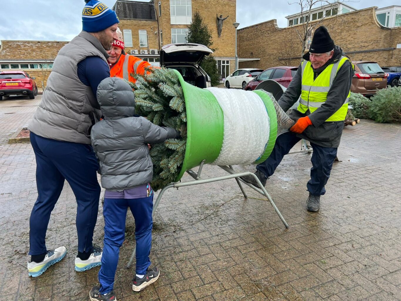 Son, father and two volunteers wrapping up a christmas tree