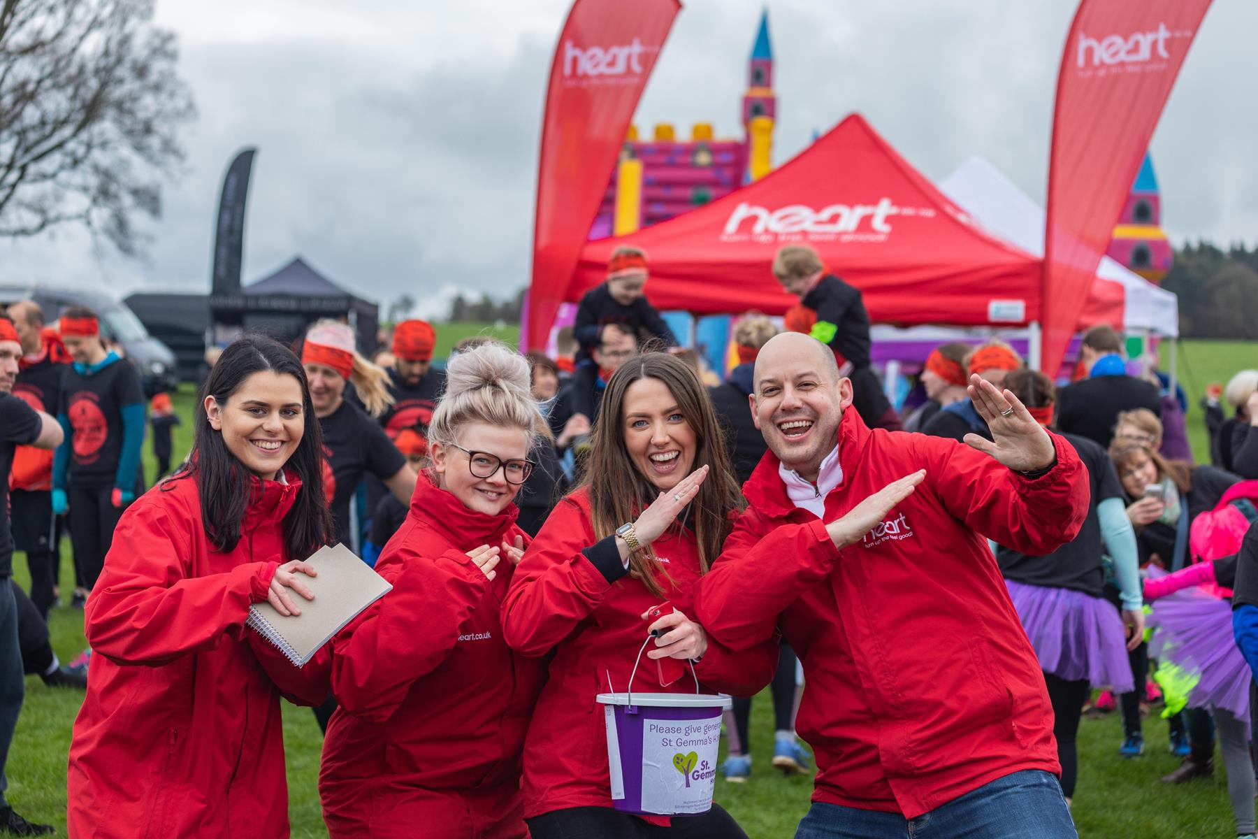 Four people wearing red Heart Radio jackets, with Heart Radio gazebo in the background