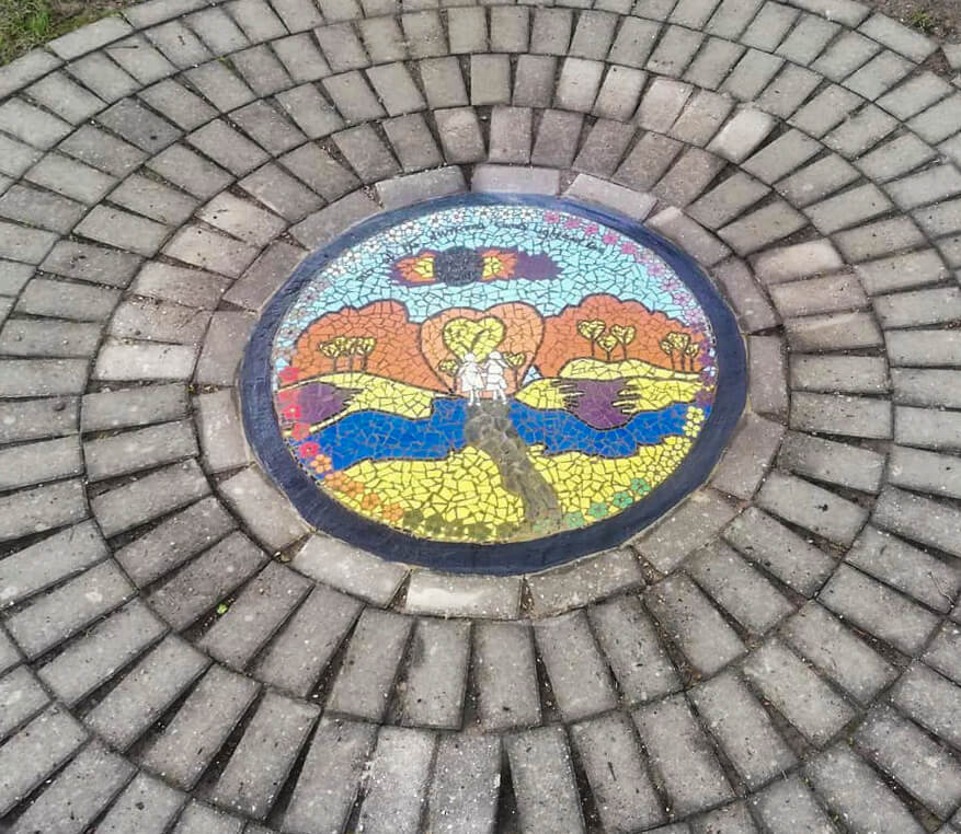 Zoomed out view of a circular mosaic on the ground surrounded by paving bricks.