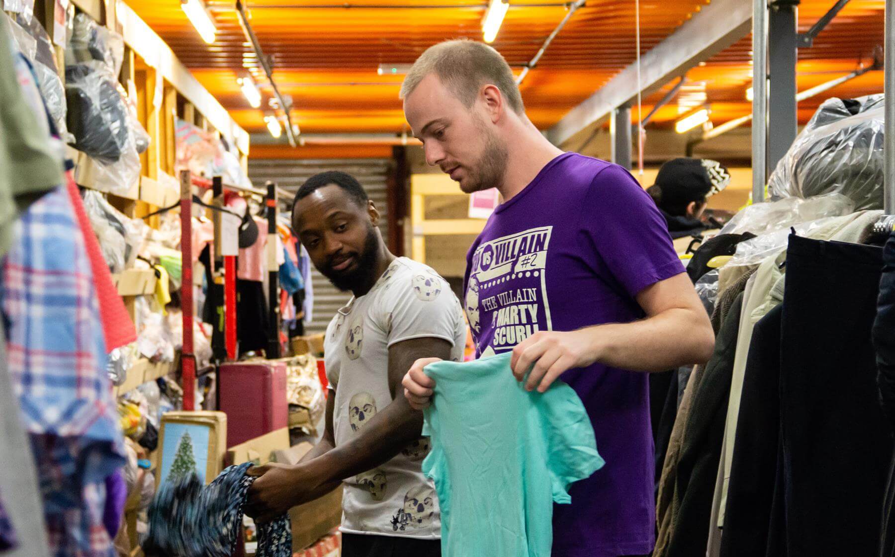 Two young men sorting donated clothes in warehouse