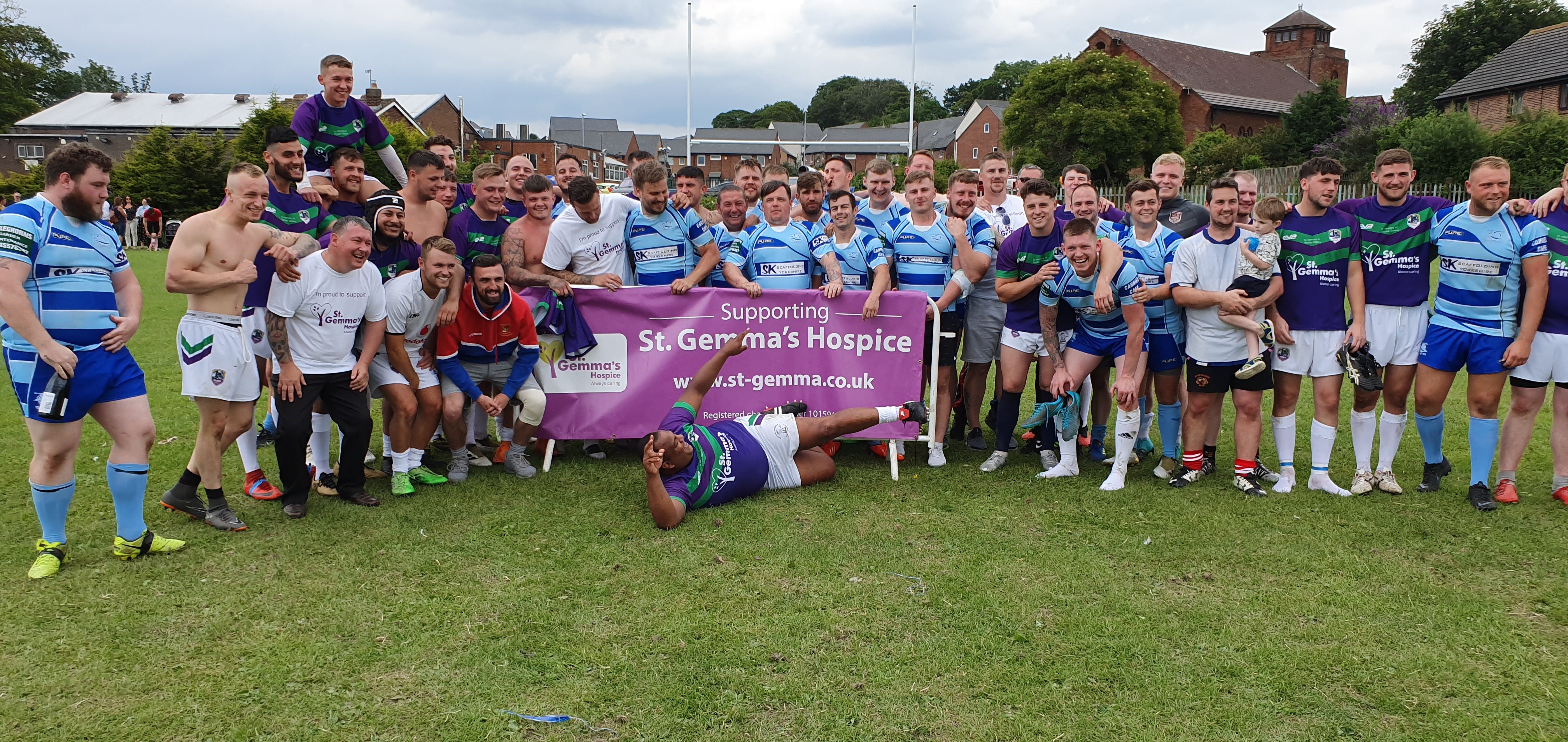 Large group of men in rugby kits holding a banner that reads: "Supporting St Gemma's Hospice".